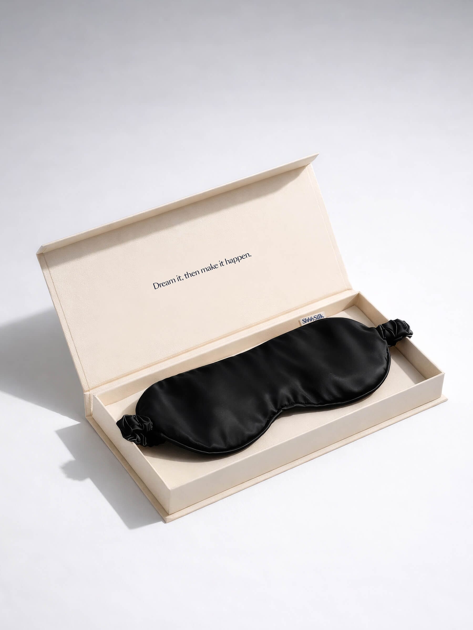 Black silk sleep mask in an open beige box on a light grey background