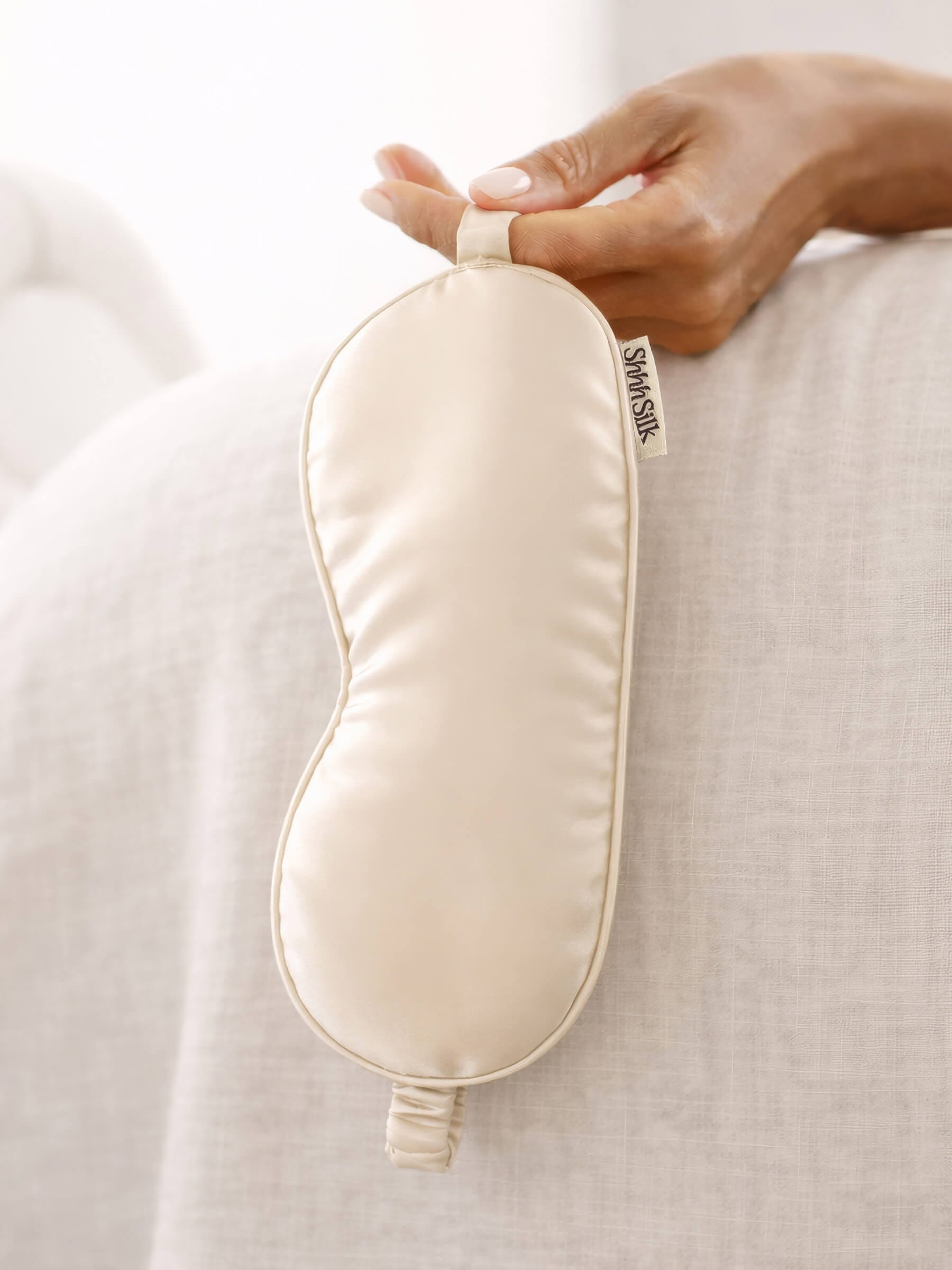 Nude silk sleep mask held by a hand on a light fabric background