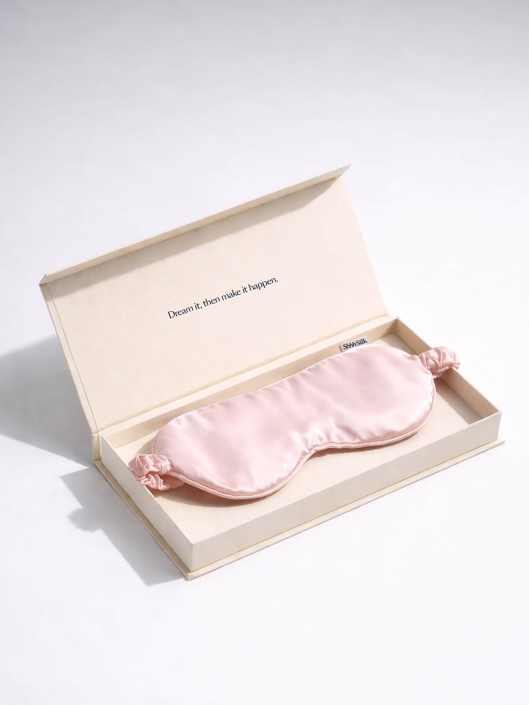 Pink silk sleep mask in an open beige box on a grey background