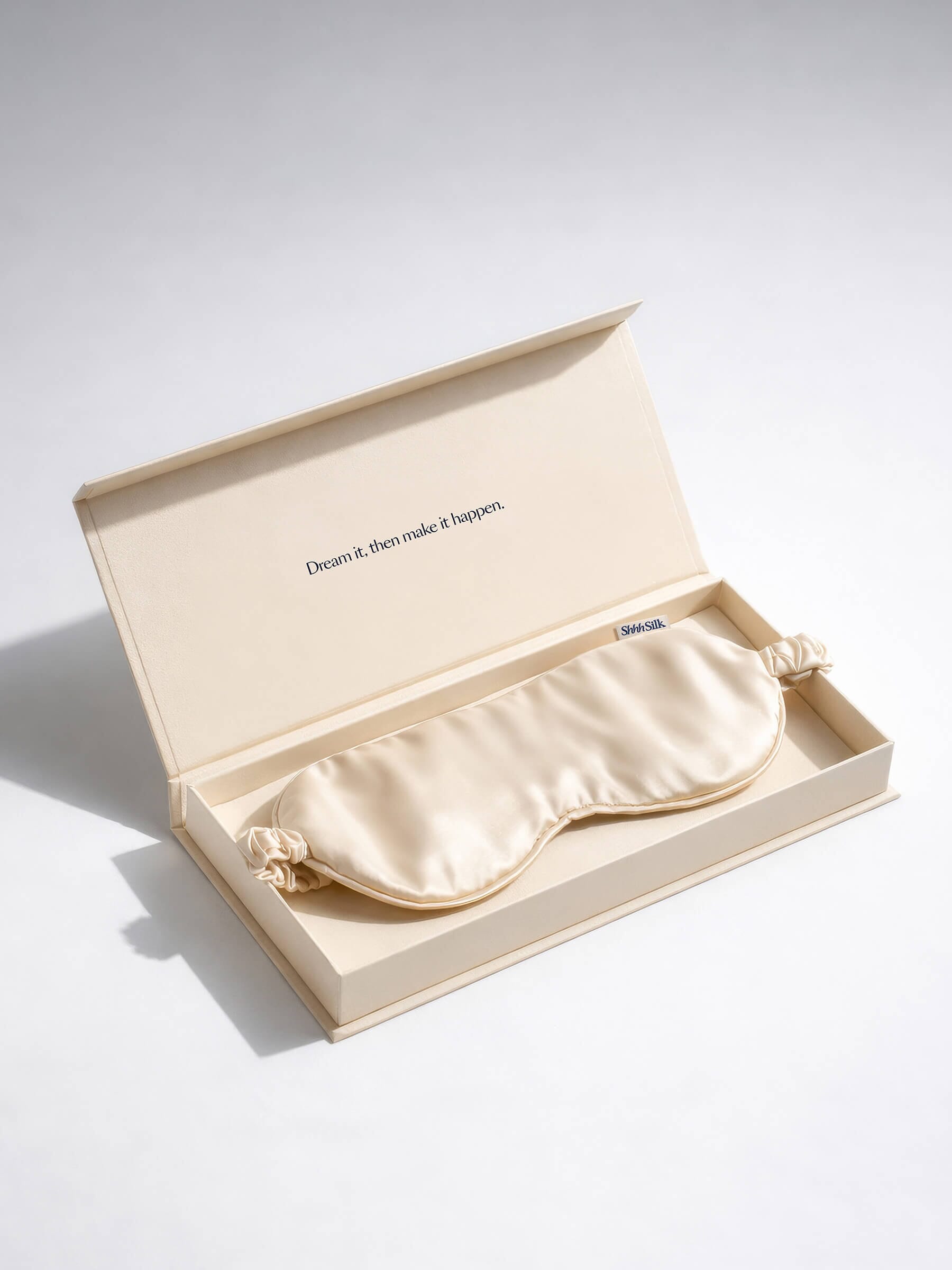 Nude silk sleep mask in an open box with a quote on a light grey background